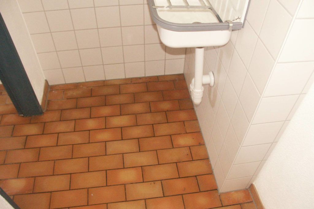 Öffentliche Toilettenecke mit weißem, wandmontiertem Waschbecken und orangefarbenen Fliesen.