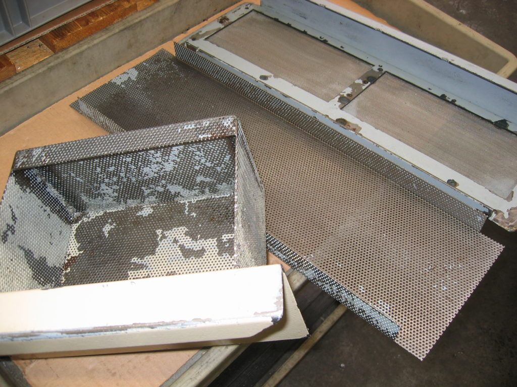 Metallgitterplatten und weiße Tafeln sind in einem werkstattähnlichen Raum auf einem Holzboden gestapelt.