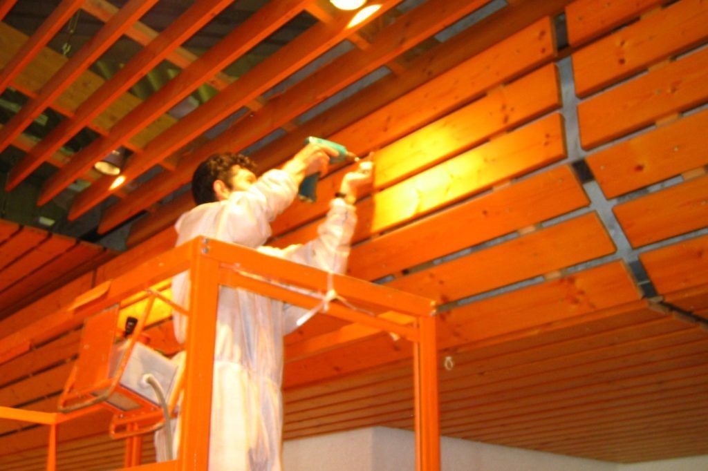 Arbeiter auf orangefarbener Hebebühne streicht eine Decke in einem unfertigen Raum
