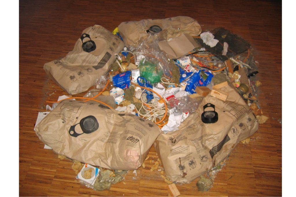 Auf einem Holzboden lagen neben beigen Bündeln mit schwarzen Klammern Plastikflaschen und Lebensmittelverpackungen.