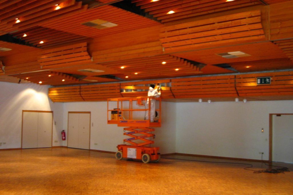 Leerer Zuschauerraum mit Holzdecke und einer orangefarbenen Scherenhebebühne in der Mitte.