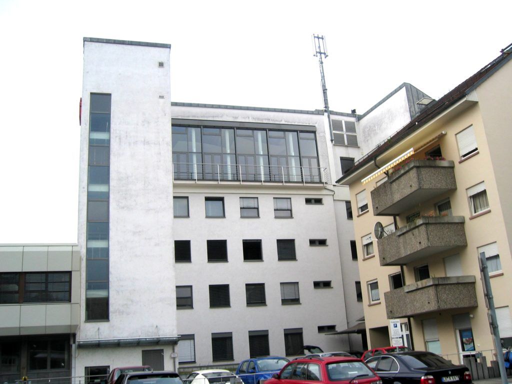 Äußeres eines Stadtgebäudes mit weißen und beigen Fassaden, Fenstern, Balkonen und darunter geparkten Autos.