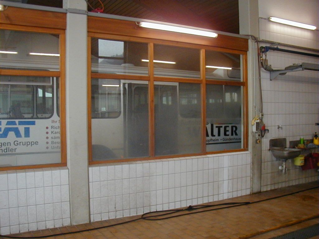 Schaufenster mit Glasfront, orange umrandeten Fenstern und weißen Fliesenwänden innerhalb eines Werkstattbereichs