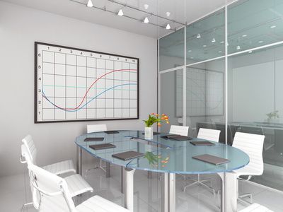 Moderner Konferenzraum mit Glastisch, weißen Stühlen, Wanddiagramm und Glastrennwand
