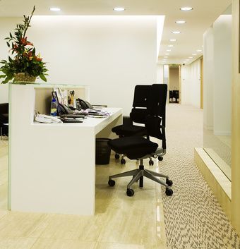 Heller, moderner Büroflur mit weißem Schreibtisch, schwarzem Drehstuhl und Topfblumen.