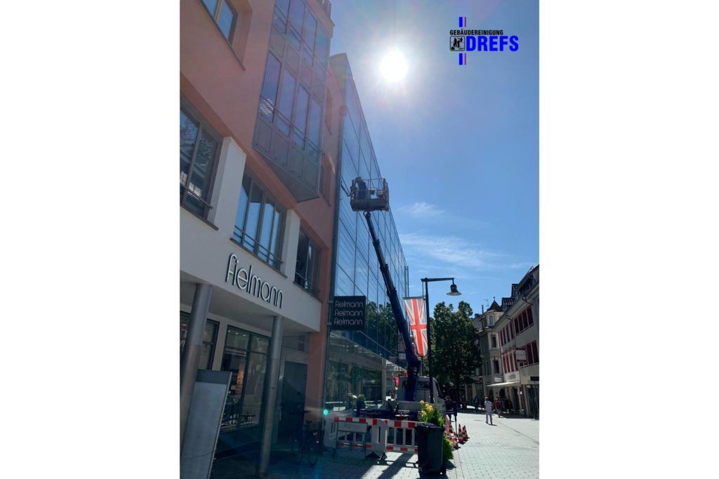 Sonnige Stadtstraße mit einem Backsteingebäude, Ladenfronten und Menschen, die draußen in der Nähe eines Cafés sitzen.