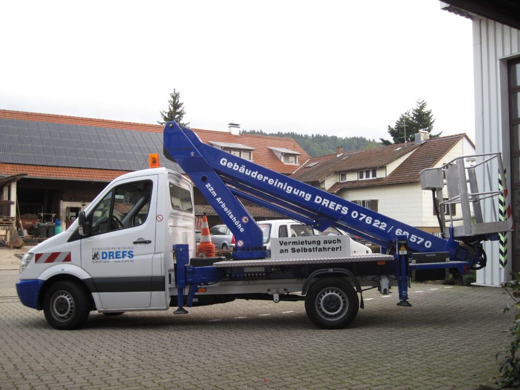 Ein blau-weißer Mobilkranwagen steht auf einem Hof, der Ausleger ist über das Fahrerhaus ausgefahren.
