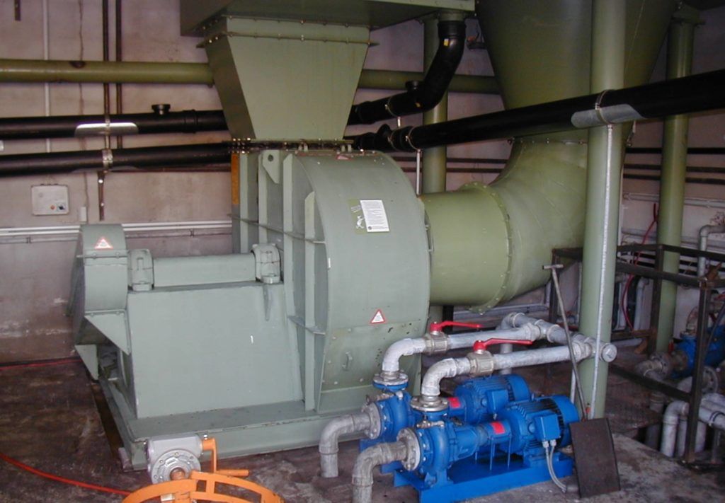 Industriemaschinen in einem Hauswirtschaftsraum, darunter ein großes grünes Gebläse sowie blaue Rohre und eine Pumpe.