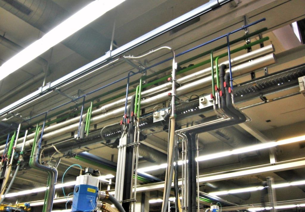 Industriedecke mit silbernen Rohren, Kabeln und Leuchtstoffröhren in einem Fabrik- oder Lagerhaus-Interieur