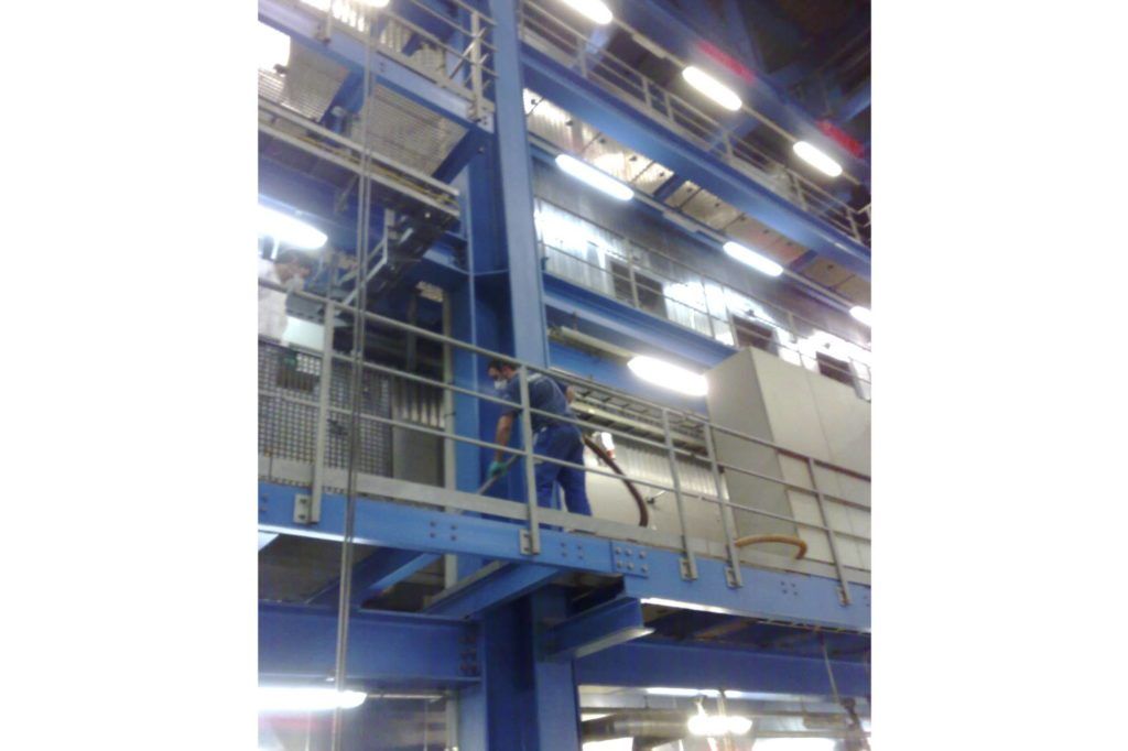 Große blaue Industriemaschine in einer Fabrik mit Deckenbeleuchtung und Metallgeländern.