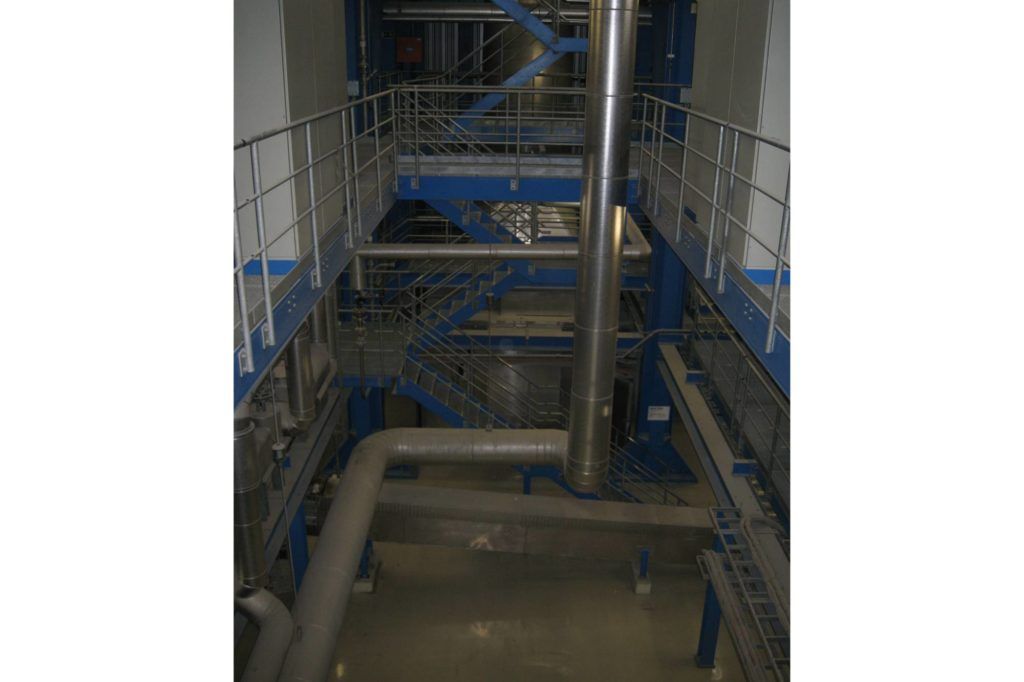 Industrielles Interieur mit blauen Metallstegen, Rohren und Maschinen in einer schwach beleuchteten Anlage