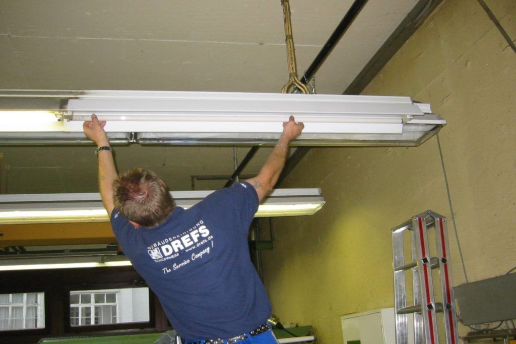 Eine Person hebt eine Leuchtstoffröhre in der Nähe der Decke in einem Raum mit einer Leiter an.