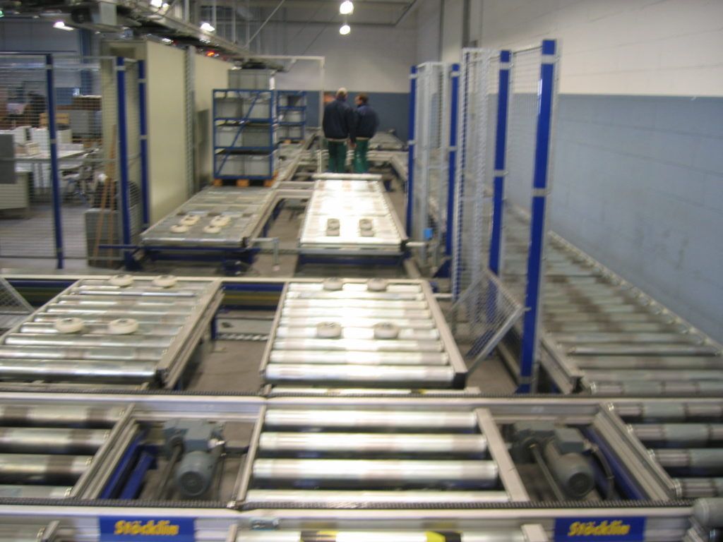 Industrielles Fördersystem in einem Lagerhaus mit Metallrollen und blau-weißen Gerätegestellen.
