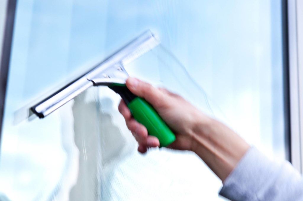 Fensterreinigung per Hand mit einem Abzieher mit grünem Griff