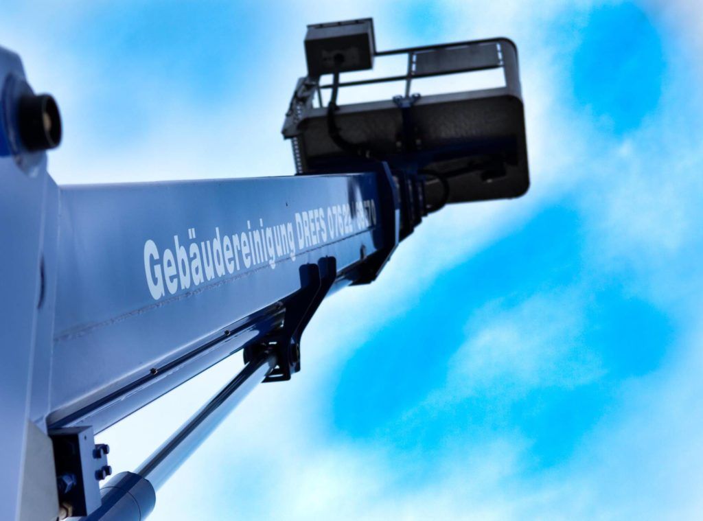 Blauer Kranarm mit Arbeitskorb vor strahlend blauem Himmel