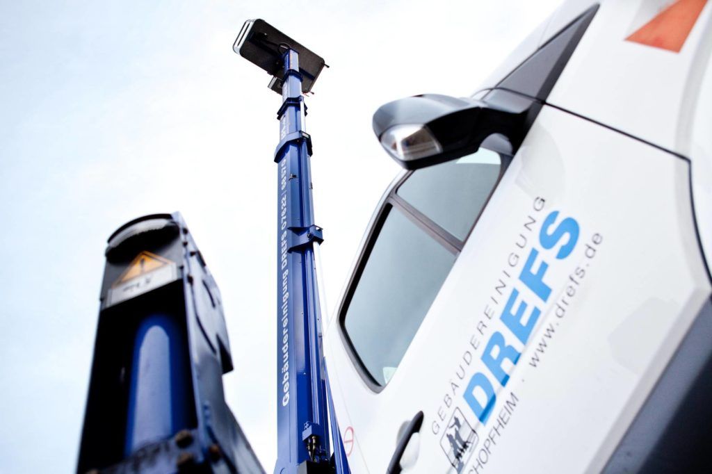 Blaue Hubarbeitsbühne neben einem weißen LKW mit „DREFS“-Logo, Aufnahme von unten