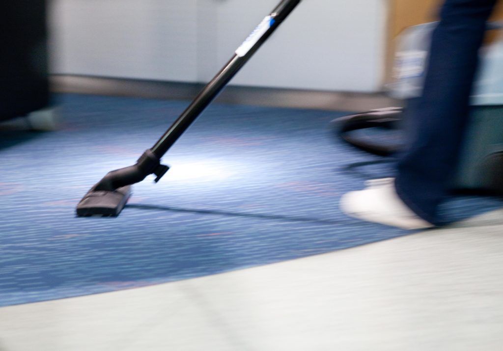 Staubsaugerdüse auf blauem Teppich neben den Beinen einer Person und weißen Schuhen