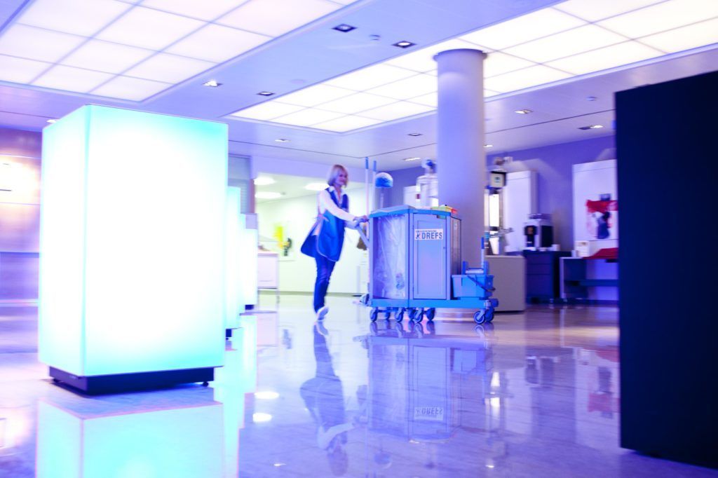Helle Krankenhauslobby mit einer Person, die unter blauem Licht einen Reinigungswagen schiebt.