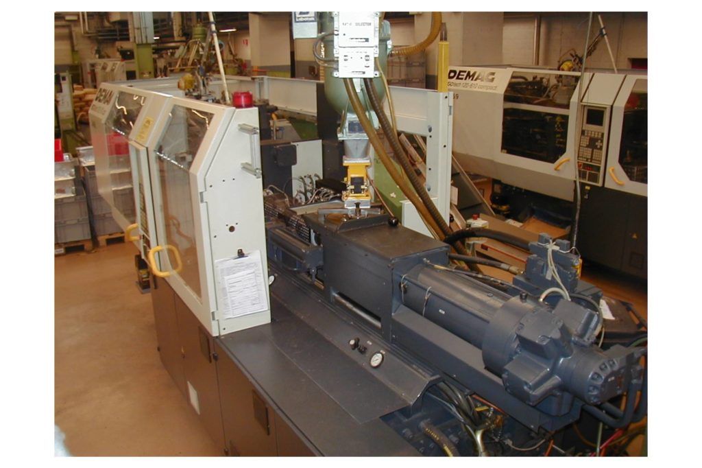 Große Industriemaschine in einer Werkstatt, mit weißen Paneelen und blauen mechanischen Bauteilen auf einem Fabrikboden