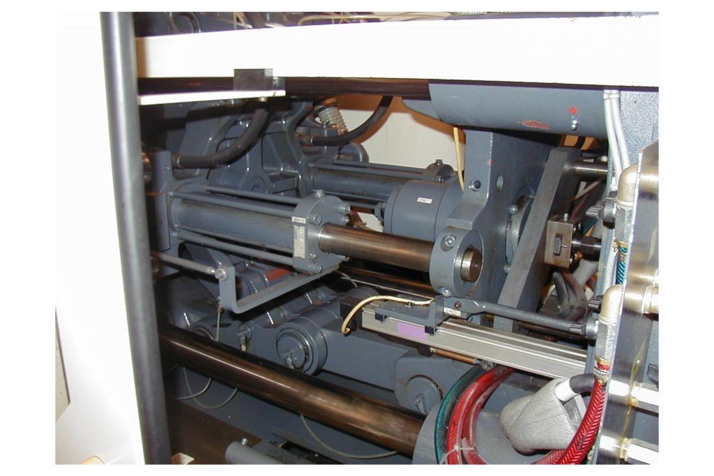Mechanische Bauteile im Inneren einer offenen Verkleidung mit Rohren, Kabeln und einer grauen Metallkonstruktion.