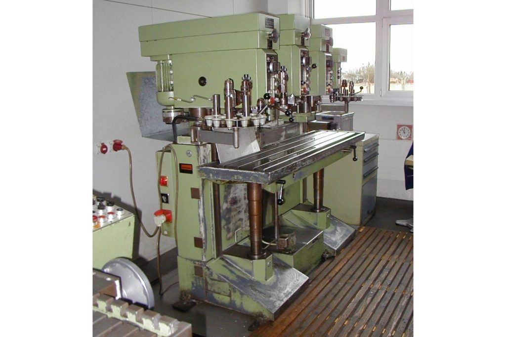 Industrielle Druckmaschine in einer Werkstatt, mit Maschinen aus grünem Metall und einer Reihe von Druckköpfen.
