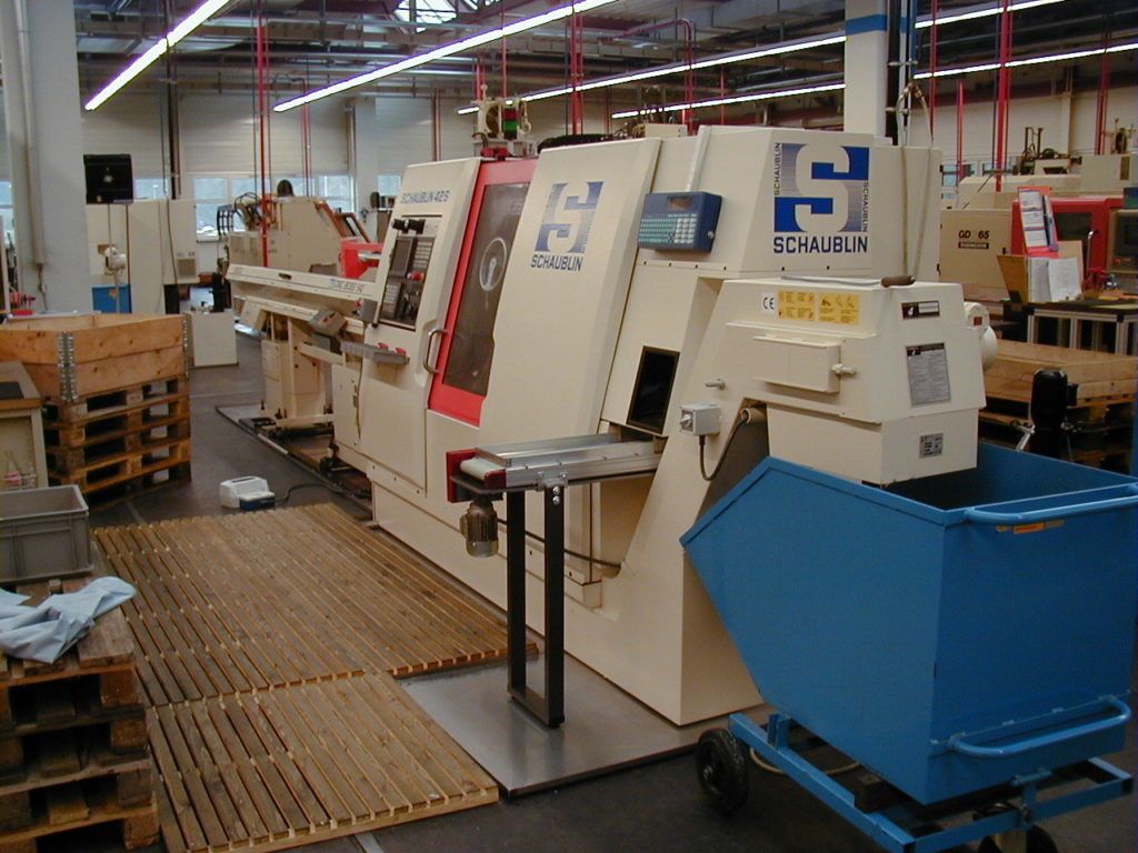Industriewerkstatt mit einer großen Maschine und einem blauen Mülleimer neben einem Holzsteg