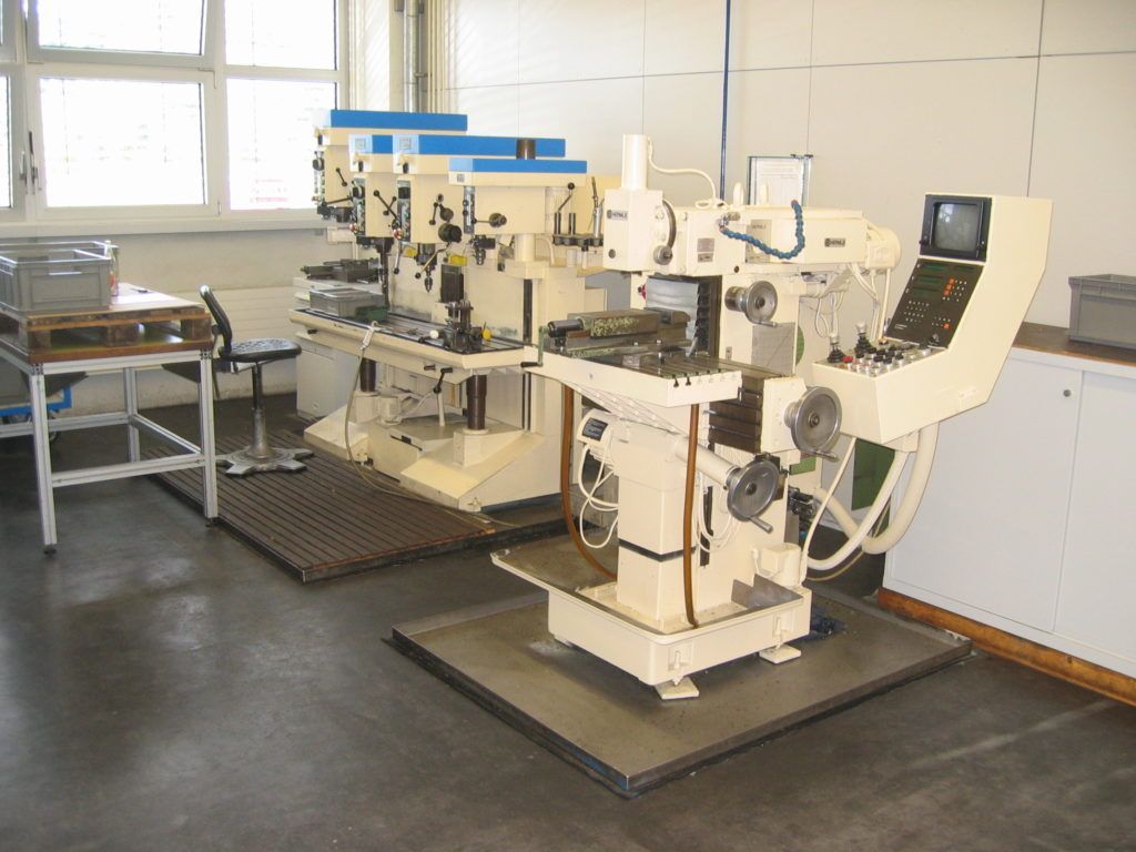 Industriemaschinen in einer Werkstatt, mit Metallgeräten und einem kleinen Monitor in der Nähe eines Fensters.
