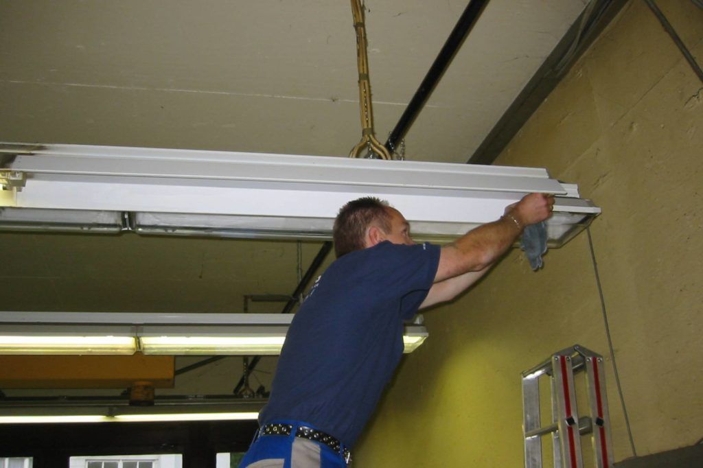Ein Mann installiert eine Leuchtstoffröhre an der Decke eines Zimmers mit gelben Wänden