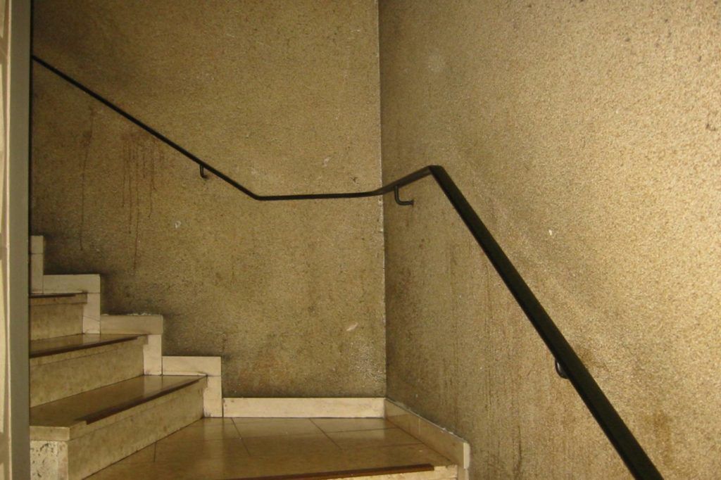 Innentreppenhaus mit beigen Wänden, weißen Stufen und einem schwarzen Handlauf um eine Ecke
