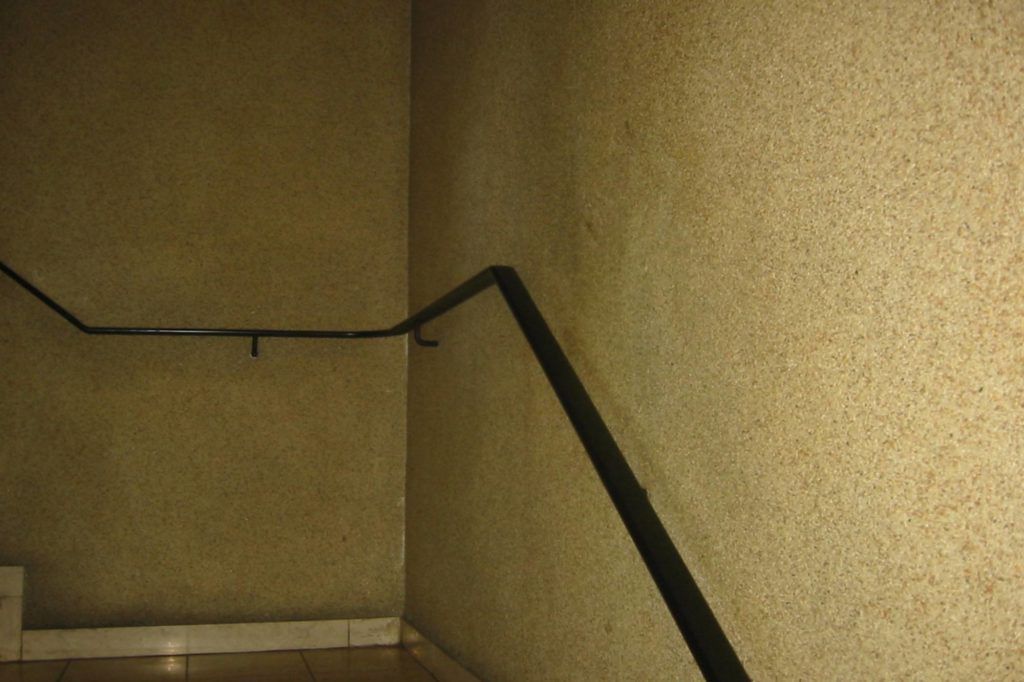 Dunkles Treppenhaus im Innenbereich mit beigen Wänden und einem schwarzen Handlauf um eine Ecke.