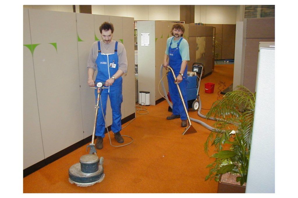 Zwei Arbeiter in blauen Uniformen reinigen einen Flurboden mit Poliermaschinen.