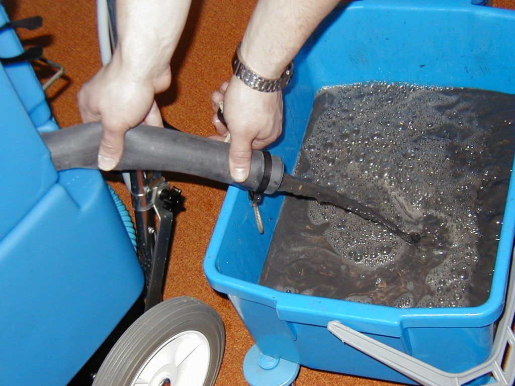 Hände beladen mit einem Schlauch einen blauen Wagen mit dunklem Kies.
