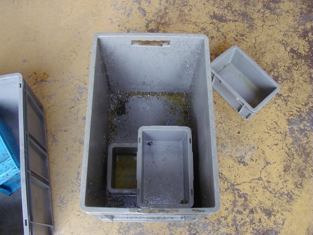 Draufsicht auf drei Plastikbehälter in einem größeren grauen Container auf einem gesprenkelten Boden.