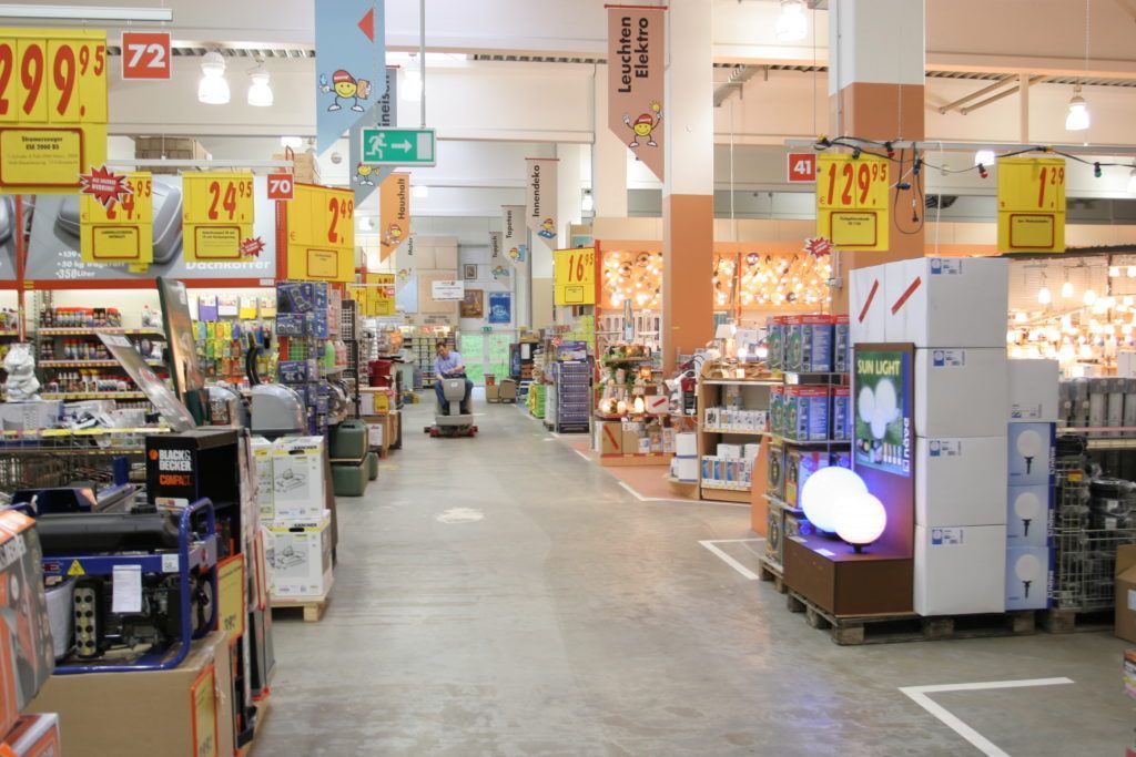 Ein Supermarktgang mit Preisschildern, vollen Regalen und einem hellen Gang, der nach hinten führt.