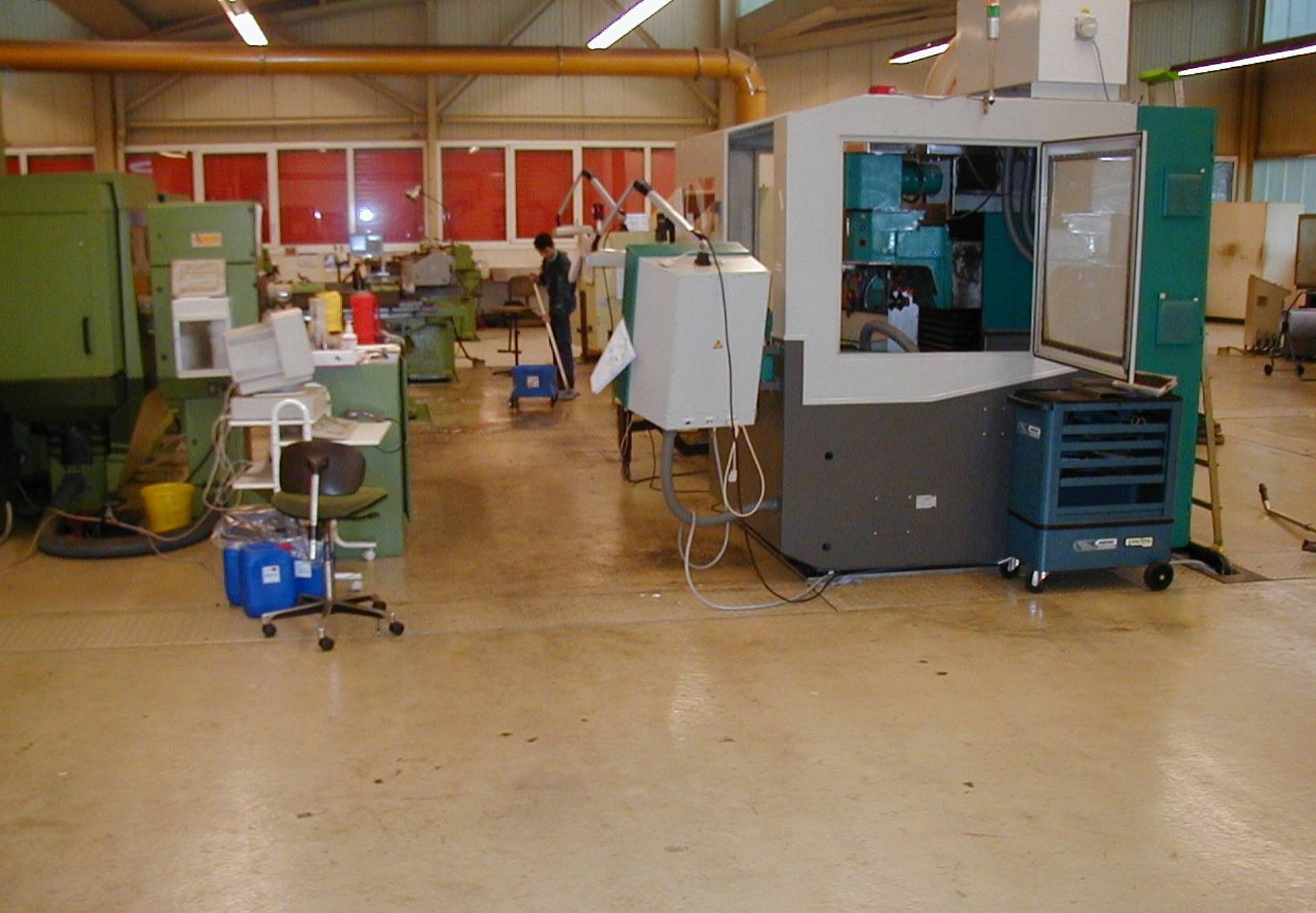 Industriewerkstatt mit großen Maschinen, Werkzeugen und einer im Hintergrund arbeitenden Person