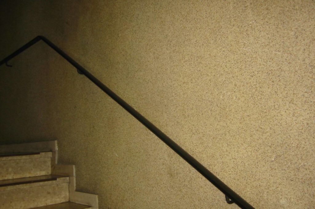 Treppe mit schwarzem Handlauf an einer beigefarbenen, strukturierten Wand.