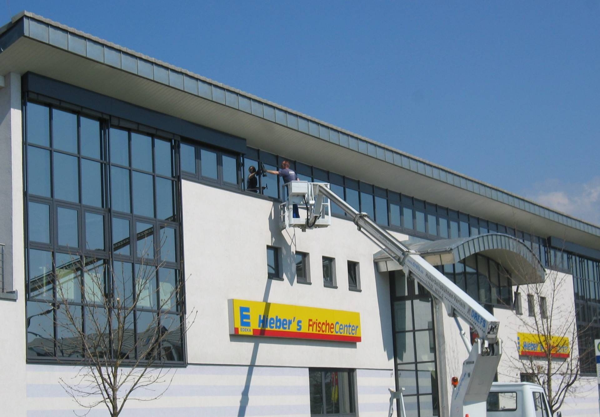 Modernes Gebäudeäußeres mit großen Glasfenstern und weißer Fassade, betrachtet an einem sonnigen Tag