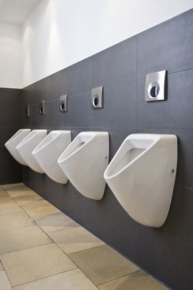 Eine Reihe weißer Urinale in einer gefliesten öffentlichen Toilette mit grauen Wänden und beigen Bodenfliesen.