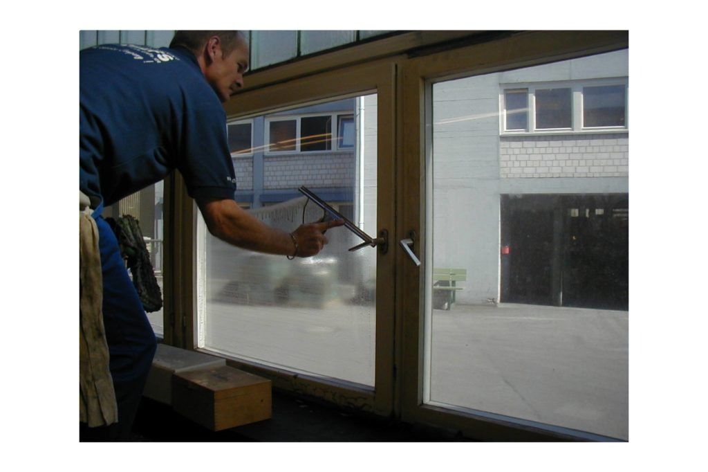 Eine Person reinigt in einem Schaufenster mit einem Abzieher ein Fenster.