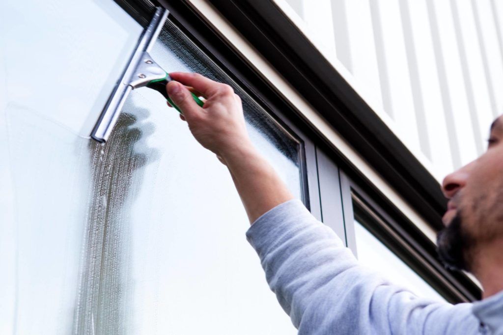 Eine Person putzt im Freien ein Fenster mit einem Abzieher.