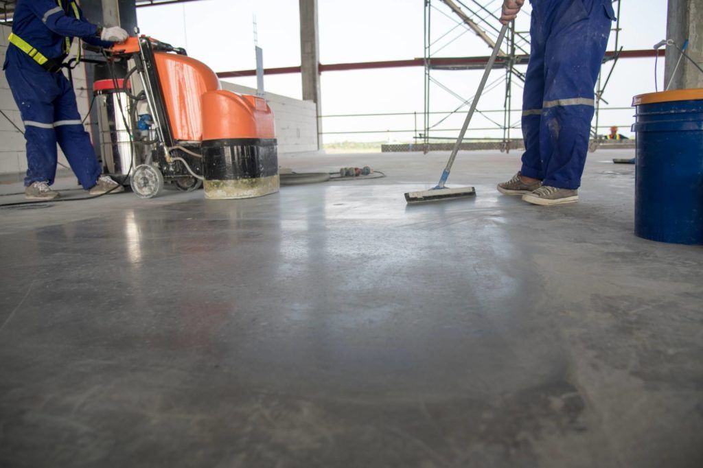 Arbeiter polieren einen Betonboden mit einer Bodenschleifmaschine in einem Industriebereich
