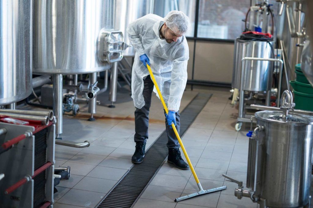 Ein Arbeiter in weißem Overall wischt einen nassen Industrieboden in einer Edelstahlanlage.