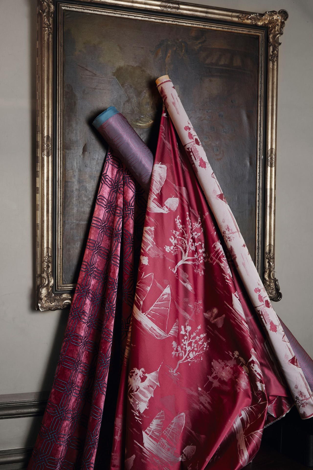 Drei Stoffrollen hängen an einer Wand vor einem Gemälde.