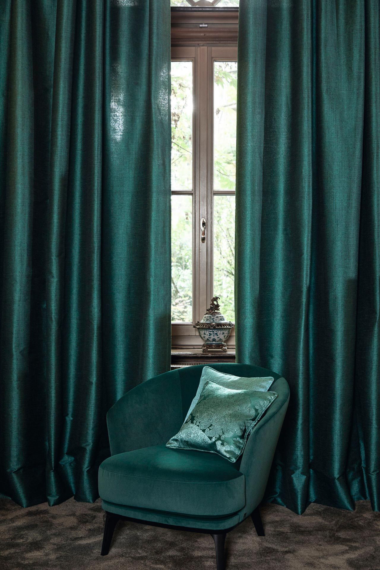 Ein grüner Stuhl steht vor einem Fenster mit grünen Vorhängen.