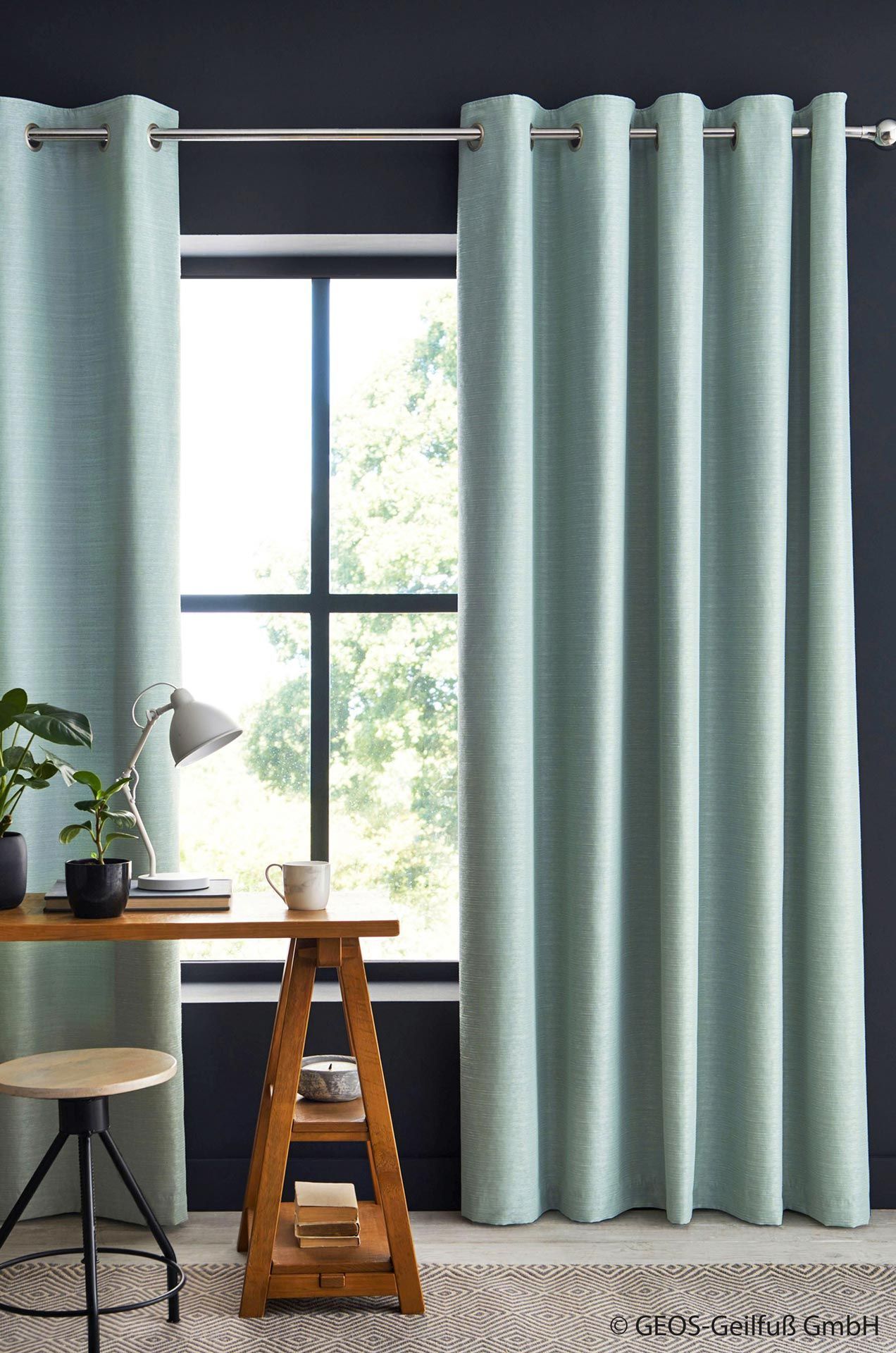 Ein Zimmer mit Fenster, Schreibtisch, Stuhl und Vorhängen.