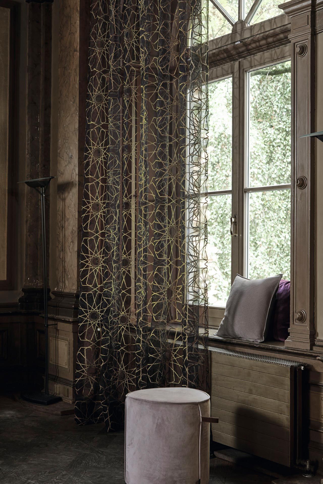 Ein Wohnzimmer mit einem Fenster und einem Hocker davor.