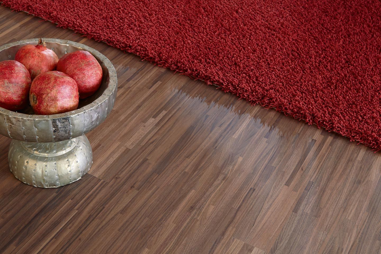 Eine Schale mit Äpfeln steht auf einem Holzboden neben einem roten Teppich.