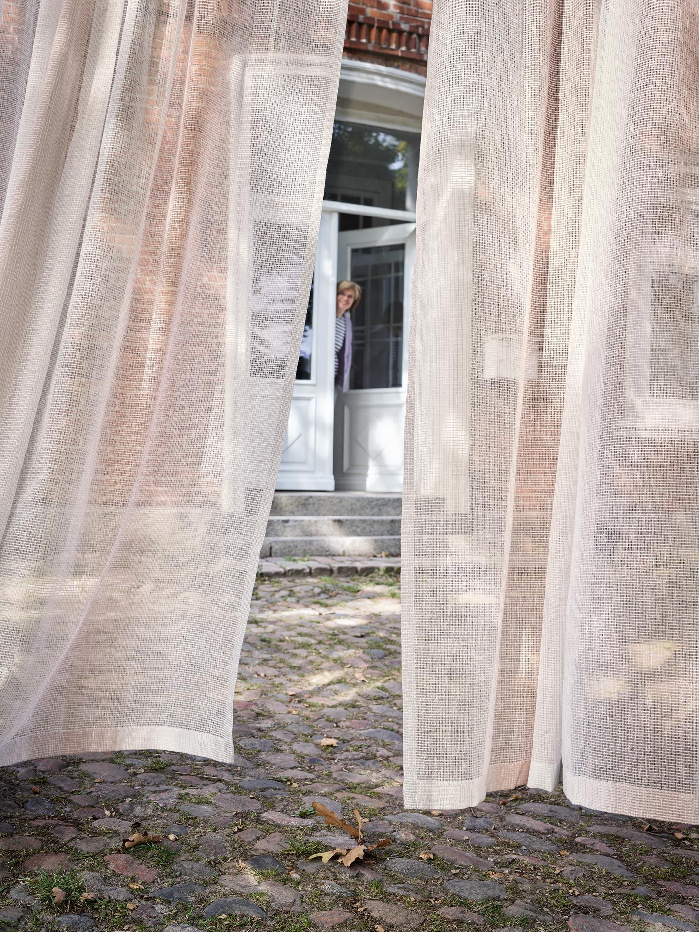 Eine Frau steht in einer Tür hinter zwei Vorhängen.