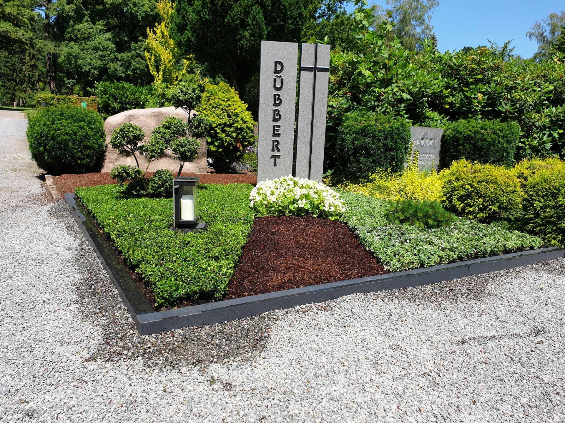 Bepflanztes Grab mit Kerzenhalter und Grabstein.