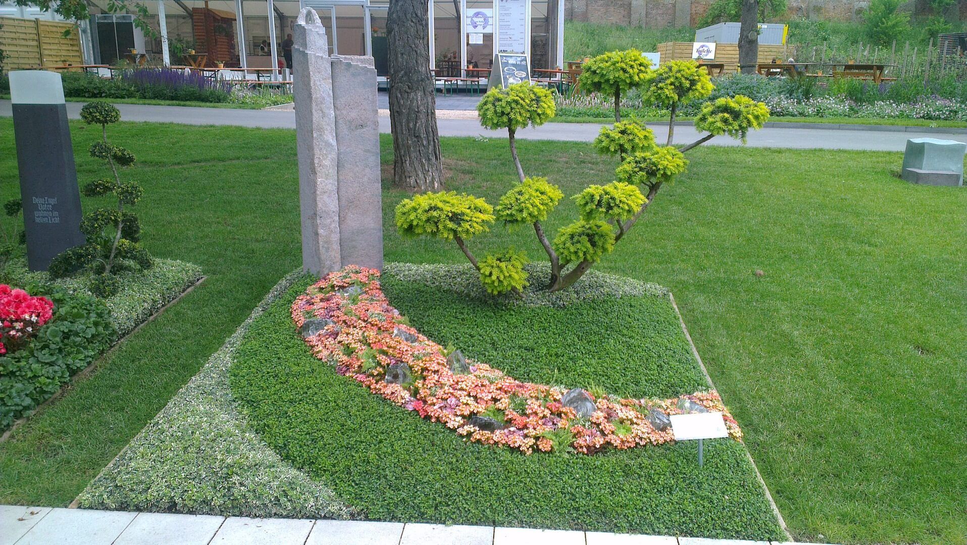 Begrüntes Grab mit Bäumchen und Blumendekoration